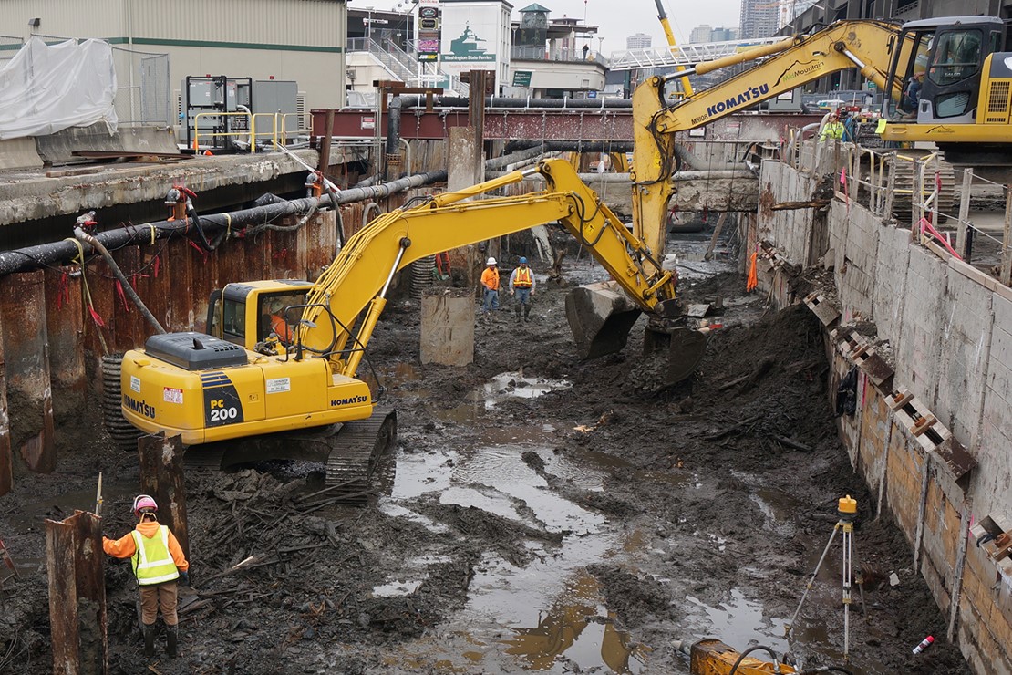 Photo shows excavator digging out muck to get to the old seawall’s relieving platform. 