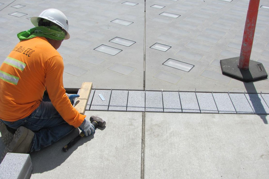 Photo shows a crew member measuring a piece of the sidewalk that will be restored. 